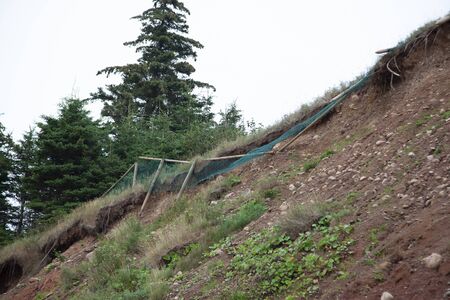 wooden fence with mesh netting has started to fall down the side of a cliff as the rockface erodes
