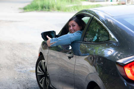 woman gives a thumbs up as she takes her car and leaves townの写真素材