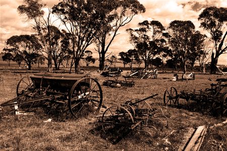 high contrast sepia image of old machinery scattered around a farmers paddockの写真素材