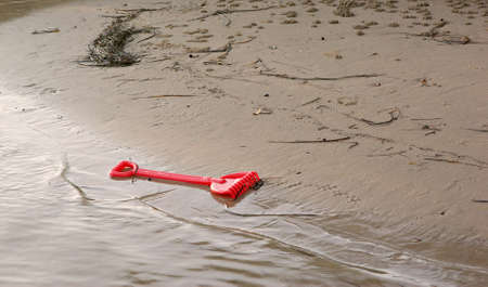 a small childs plastic rake is left behind as the tide comes inの写真素材