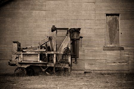 an old baler in front of a barn on the farm in sepia の写真素材