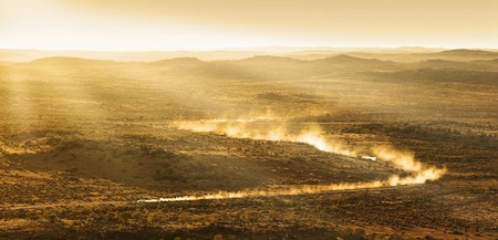 two cars leave plumes of dust as they go through the desert at sunsetの写真素材