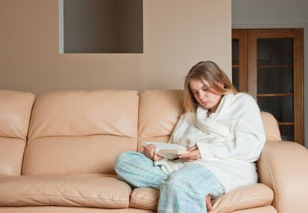young woman reading a book on sofaの写真素材