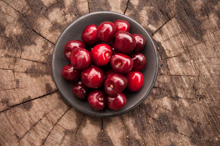 black cup with cherry on old tree stump texture backgroundの写真素材