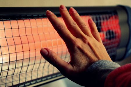 Infrared heater in the house. A woman warms his hands.の写真素材