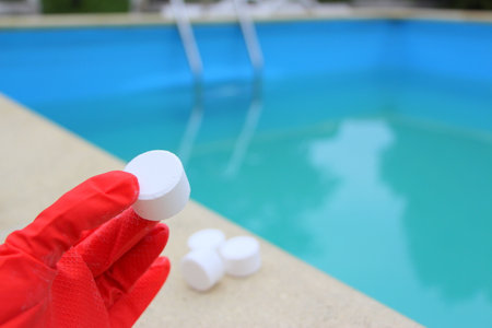 White mini-tablet of chlorine in the hand of the staff for disinfection of swimming pools. The...