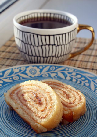 Sponge roll with apricot jam on a blue plate and a cup of coffeeの写真素材