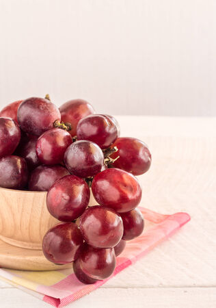 Red grapes in wooden bowl on a wooden table backgroundの写真素材
