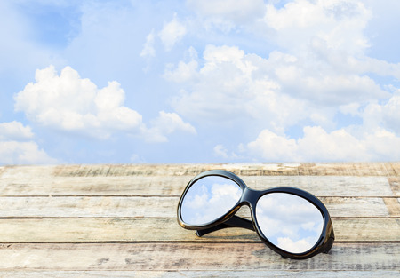 Clear sky in eyeglasses on the wooden table over blue sky backgroundの写真素材