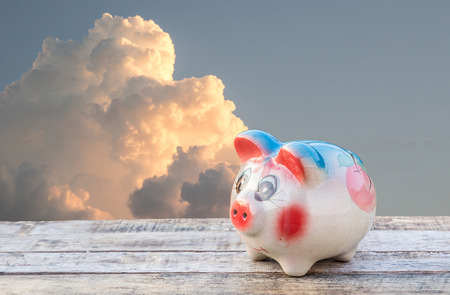 Piggy bank on wooden table over sky blurred background. saving money concept.の写真素材