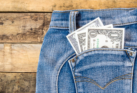 Dollar money in pocket blue jeans on wooden backgroundの写真素材