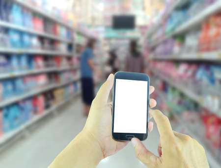 Hand holding smart phone with blurred supermarket backgroundの写真素材