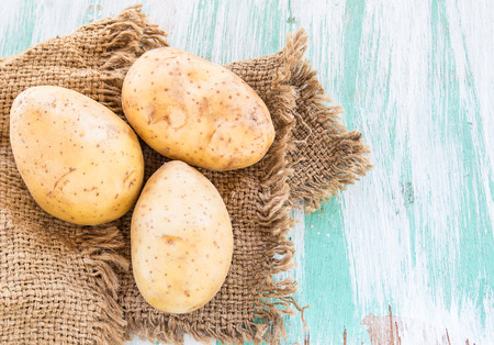 Sack fresh organic potatoes on a wooden table backgroundの写真素材