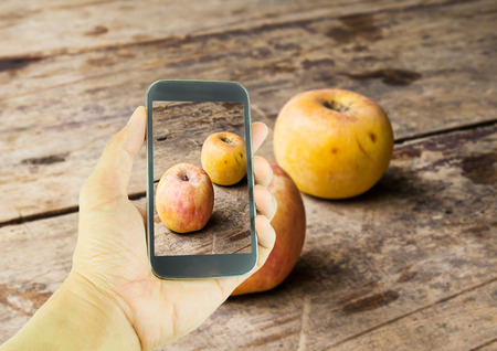 Hand holding smart phone and old apple on wooden table backgroundの写真素材