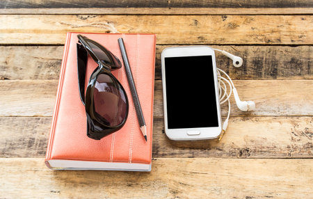 Notebook, sunglasses, smart phone and earphone on wooden table background