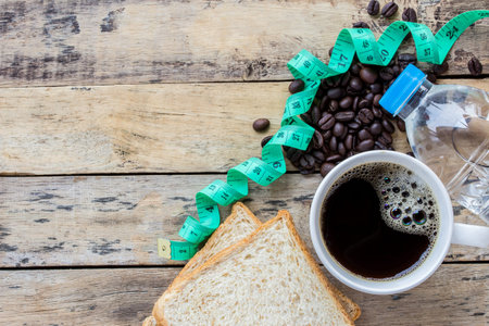 Coffee,slice of bread,measuring tape and coffee beans on wooden table backgroundの写真素材