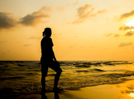 silhouette of young woman walking on beach at sunsetの写真素材