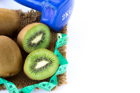 Fresh kiwi and measuring tape with blue dumbbell on sackcloth on a white background. Healthy conceptの写真素材