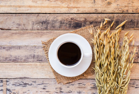 Ears of wheat and cup of coffee on a wooden table background