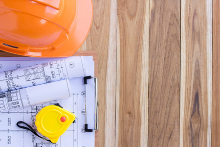 Safety helmet and tape measure over a construction plan drawing for the project engineer jobs