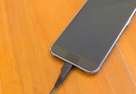 Close up of smart phone charging with USB cable on wooden texture backgroundの写真素材
