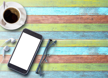Cup of coffee with smartphone,glasses and earphones on colorful wood table background with copy space for any design. smart phone and coffee cup on wooden top viewの写真素材