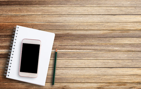 Notebook or note pad and smart phone with pencil on old wooden background top view with copy space. office desk concept.の写真素材
