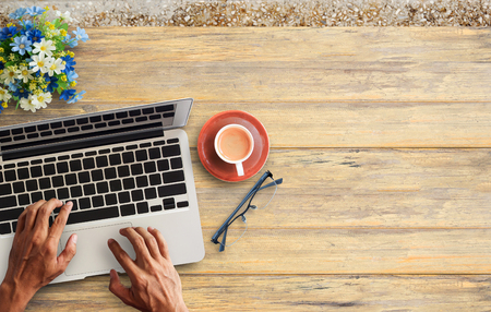 Business man hands using a laptop with cup of coffee and glasses vintage hipster wooden desktop top view with copy space. Business conceptの写真素材