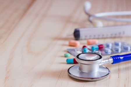 Close up blue stethoscope and pills with tablets on wooden table. Health and medical conceptの写真素材