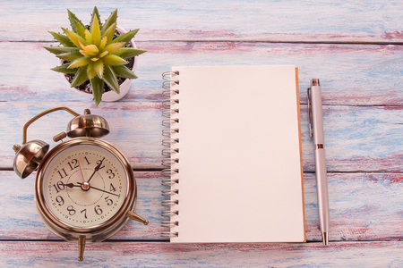 Flat lay photo with blank notebook, pen and alarm clock with flower on wooden table background. Top view with copy space for designの写真素材
