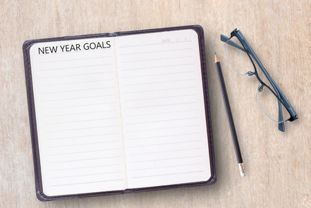 Conceptual business of notebook,black pencil and glasses on a old wooden table background. open diary and pencil with NEW YEAR GOALS words. Business and concept idea for design.の写真素材