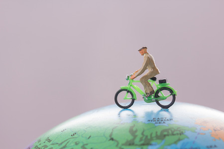 Miniature people - Figure businessmans cycling on mini globe ball model with blurred background. Business finance and travel concept.の写真素材