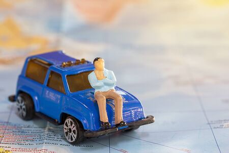 Miniature people : business man sitting on blue car for travel around the world with word map background.earth background concept.の写真素材