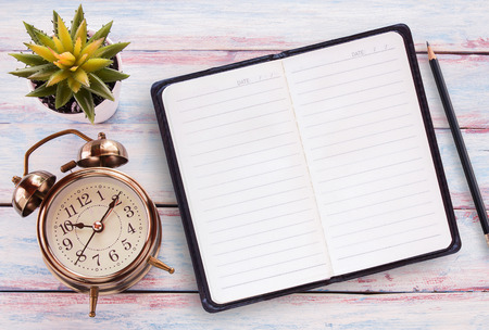 Retro alarm clock,notepad,pencil and flower on a wooden table. Photo in retro color image style. Top view with copy space for use.の写真素材