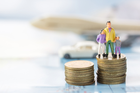 Miniature people: Family standing on the coin and blurred white airplane toy background with sunlight. using as background travel or business concept.の写真素材