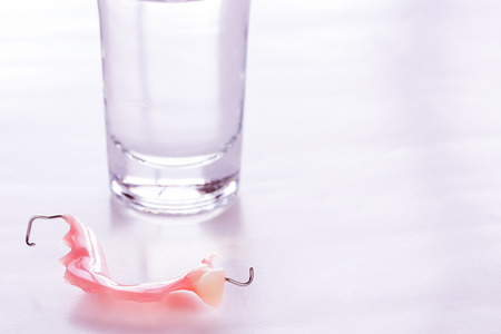 Close up acrylic dentures immersed in a glass of water,table in the bedroom. Bright simple background.の写真素材
