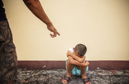 A finger pointing at a child sit on the floor and a little Asian boy doing sadの写真素材