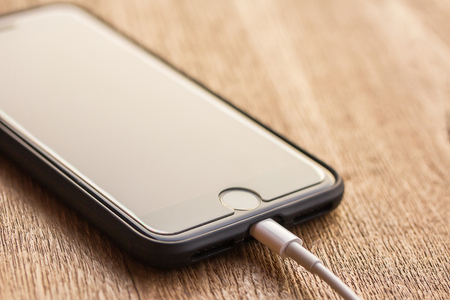 PHARE, THAILAND -FEBRUARY 23, 2018: close up image of the new phone with the charging cable on the wooden table on February 23, 2018 in Phare Thailand.のeditorial素材