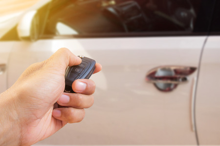 Men's hand presses on the remote control car alarm systems with sunlight and blur car background.の写真素材