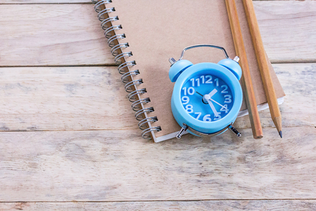Top view with blank empty notepad, alarm clock and pencil on wood table. Office desk or work placeの写真素材