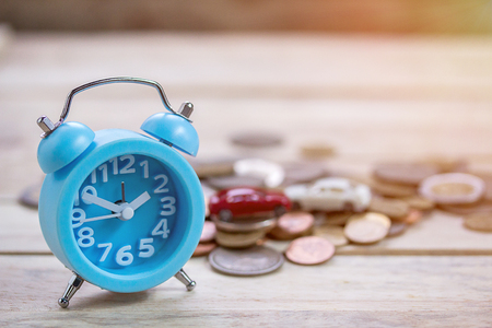 Coins and blue alarm clock on wood tableの写真素材
