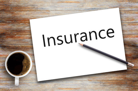 Insurance text on white paper,notepad or notebook with black pencil and cup of coffee on brown wood table background.using wallpaper for education,business photo.Take note of the product for book with paper and concept. object or copy space for design.の写真素材