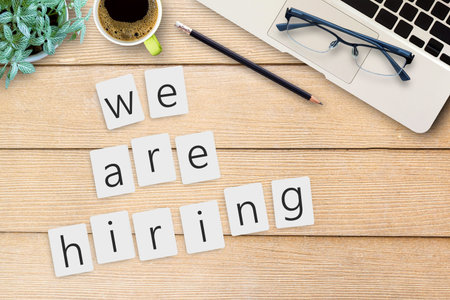 We are hiring text on sticky notes on office desk table with laptop computer, black pencil,glasses and cup of coffee. Top view with copy space (selective focus). Business and workplace concept for use.の写真素材