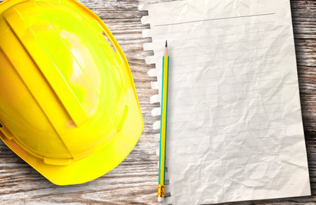 Top view of yellow safety helmet hat and blank paper with pencil in the project at construction site building on wood table background. helmet for workman as engineer worker. concept safety firstの写真素材