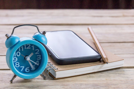 Office desk with notebooks,smartphone,pencil and alarm clock on wood table in office workplace with copy spaceの写真素材