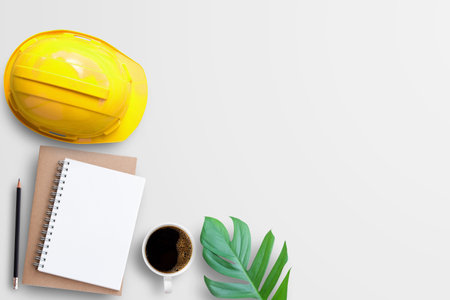 Safety helmet, notebooks,pencil,cup of coffee and fresh leaf on white table background in workplace. Top view with copy space for design. Business and industry concept.の写真素材