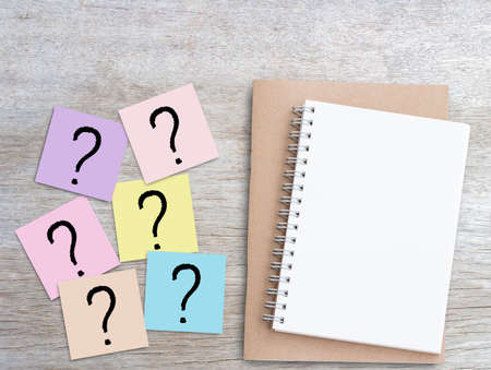 Question mark on pink sticky notes and blank notebook on wood table background. Business and education concept design.の写真素材