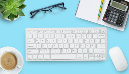 Office desk with stationary,keyboard,notebook,calculator,pencil,coffee and flower on blue table...