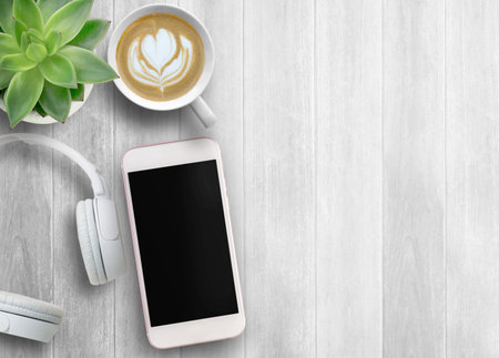 Smartphone black screen, white head phone and cup of coffee on wooden table background, mockup...