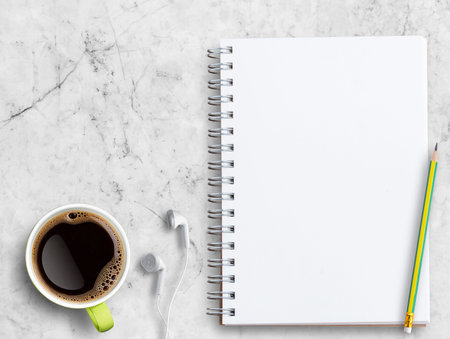 Top view blank notebook,white earphone,pencil,cup of coffee on white marble background.